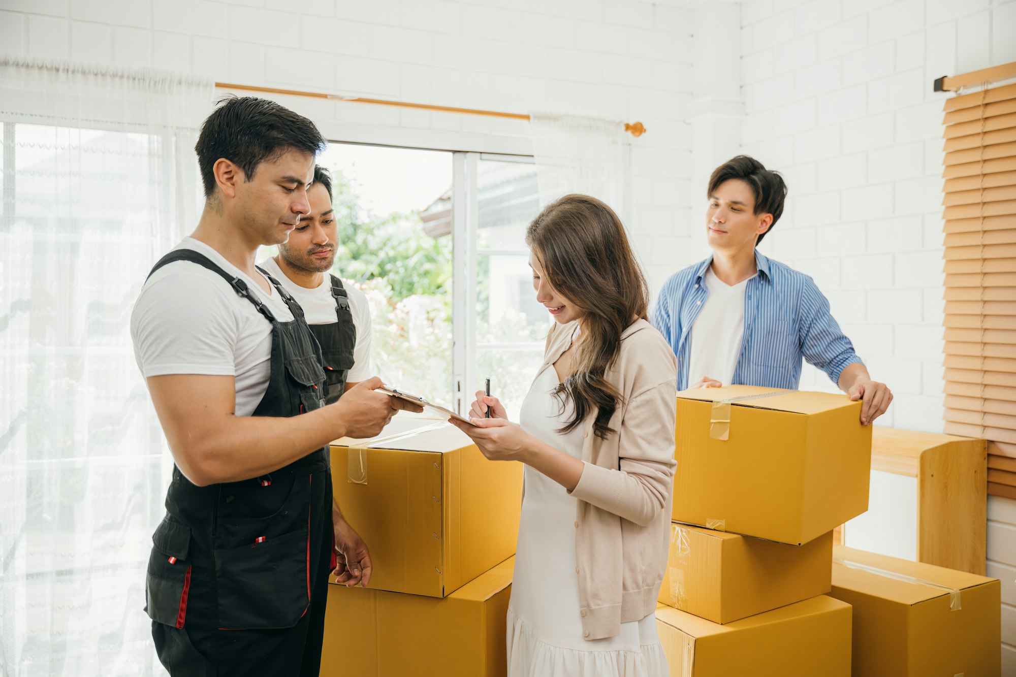 Couple inspects checklist before signing moving papers. Worker carries a box. Professional movers