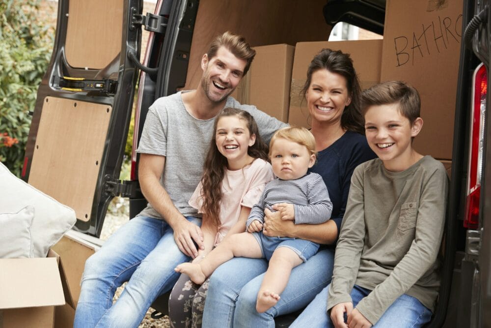 Family Sitting In Back Of Removal Truck On Moving Day