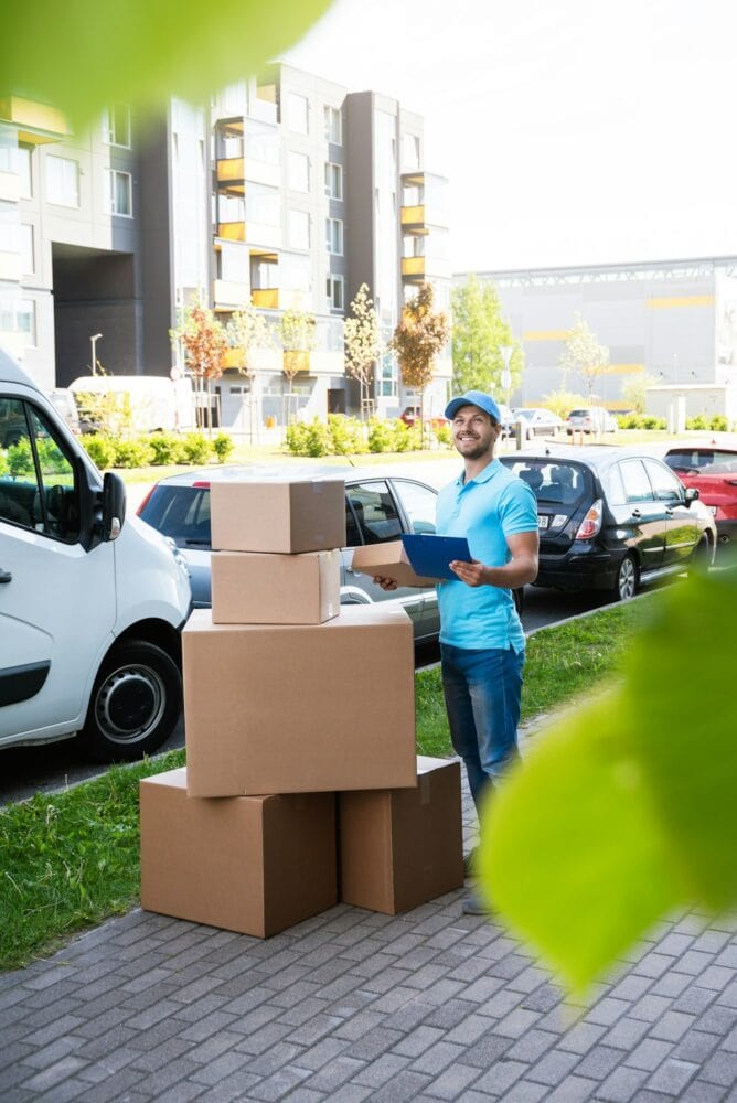 Happy delivery man with a lot of cardboard boxes near his van